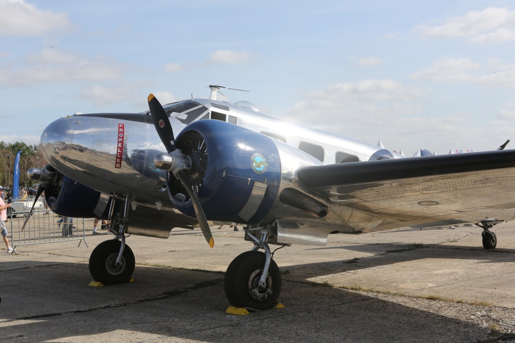 Een glanzend vliegtuig met een propeller en blauwe accenten, tentoongesteld op een vliegshow.