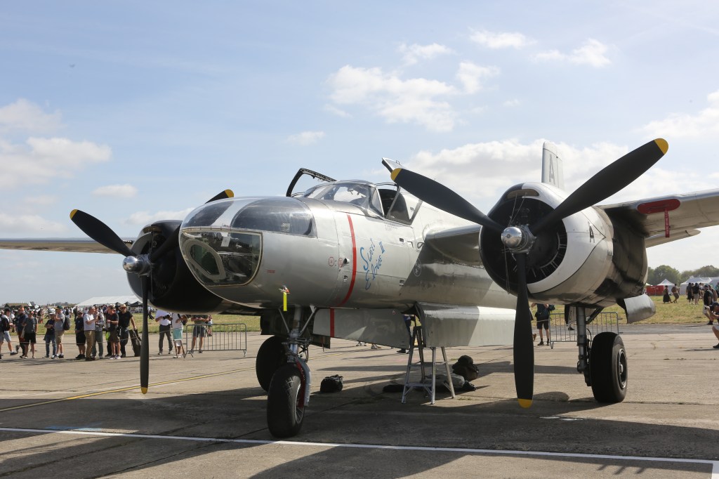 Een vintage vliegtuig met dubbele propellers, gefotografeerd op een vliegshow, met een menigte toeschouwers op de achtergrond.