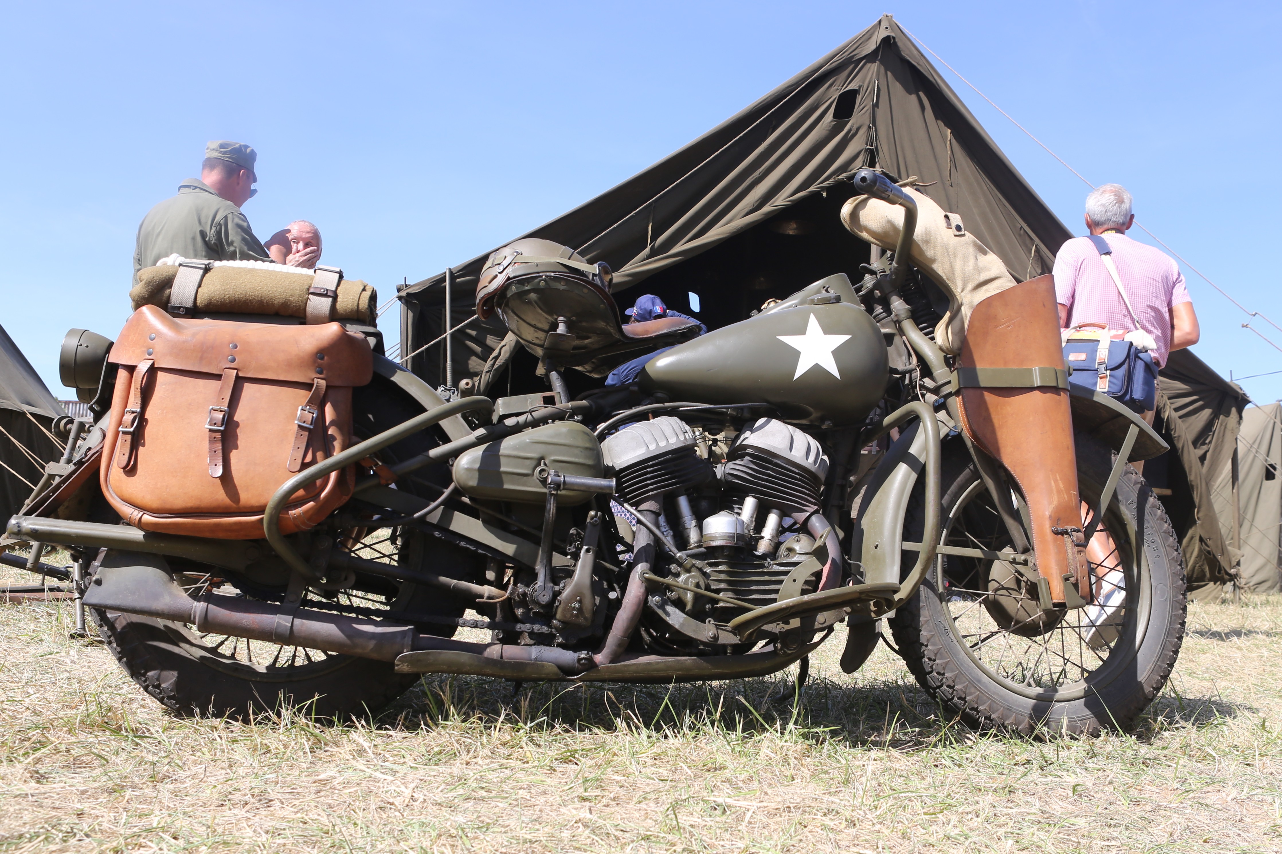 Een vintage militaire motorfiets met leer en groene camouflage, voor een tent op een evenement.