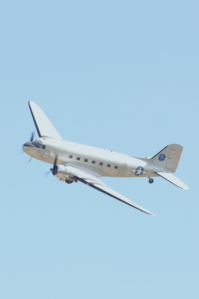 Een vintage vliegtuig vliegt tegen een heldere blauwe lucht.