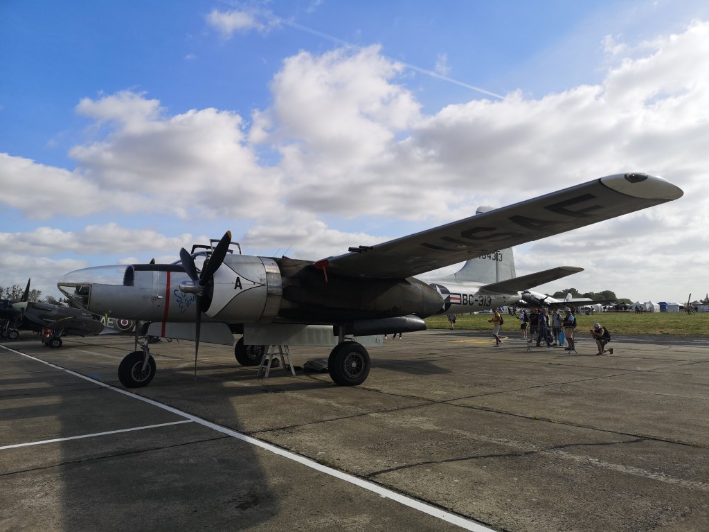 Een historische militaire vliegtuig, de B-25 Mitchell, geparkeerd op een luchtshow met mensen die het verkennen.
