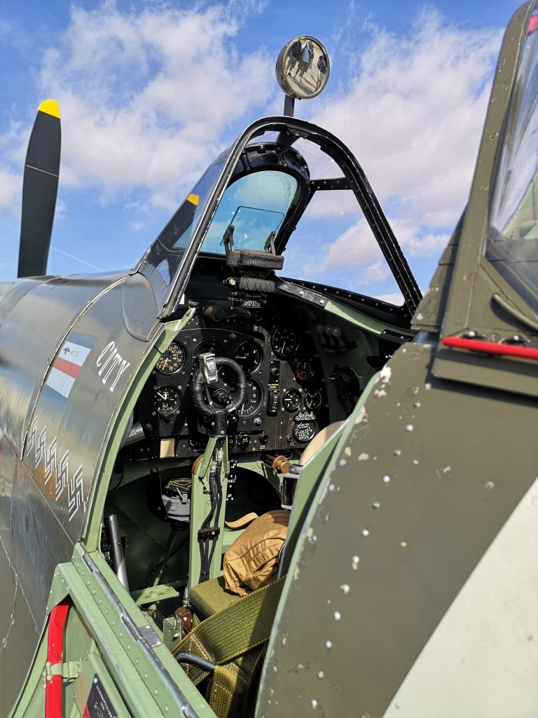Een close-up van de cockpit van een vintage vliegtuig, met een zicht op de instrumenten en controles, waaronder een stuurwiel en verschillende meters.