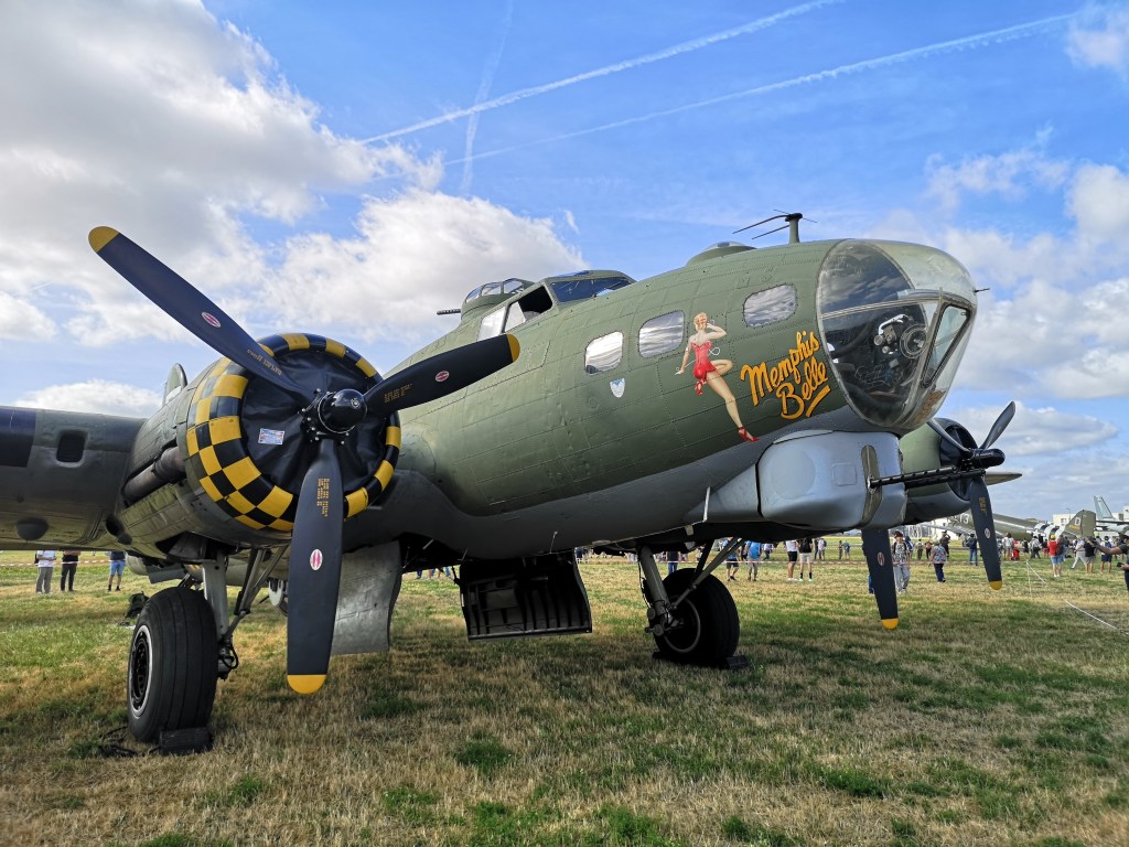 Een B-17 bommenwerper met het opschrift 'Memphis Belle', afgebeeld op een luchtshow, met duidelijke propellers en een groenverf oppervlak.