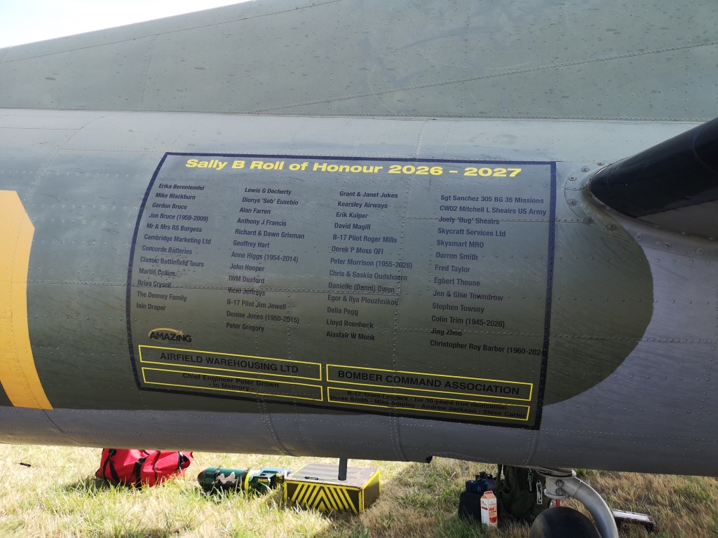 Een bord op een vliegtuig met de 'Sally B Roll of Honour 2026 - 2027', met namen van eerbetoon aan verschillende personen.