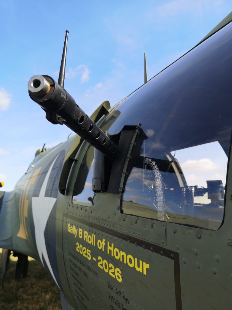 Detail van een ouderwetse vliegtuigmachinegeweer met een antenne, gefotografeerd vanaf de zijkant van een militaire vliegtuigcockpit, met de lucht op de achtergrond.