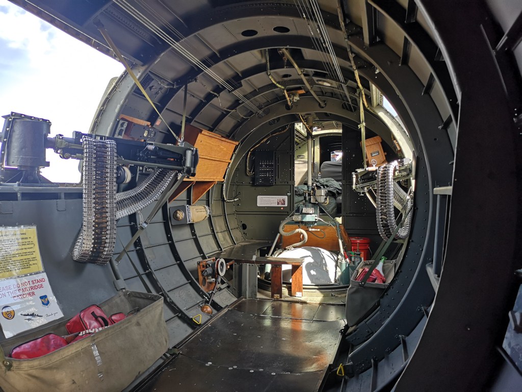 Interieur van een historische vliegtuigromp met zicht op de cockpit en uitrusting, inclusief een mitrailleur en opbergruimte.