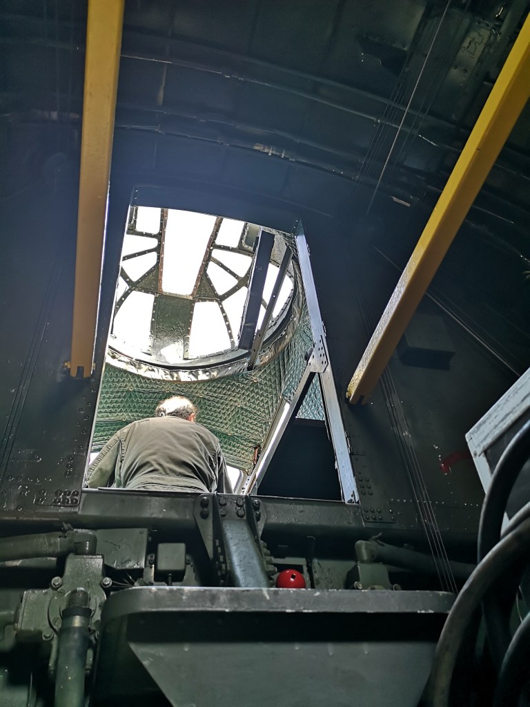 Uitzicht op een open toegang van een voertuig, met een man die naar buiten kijkt, omringd door metalen structuren en leidingen.