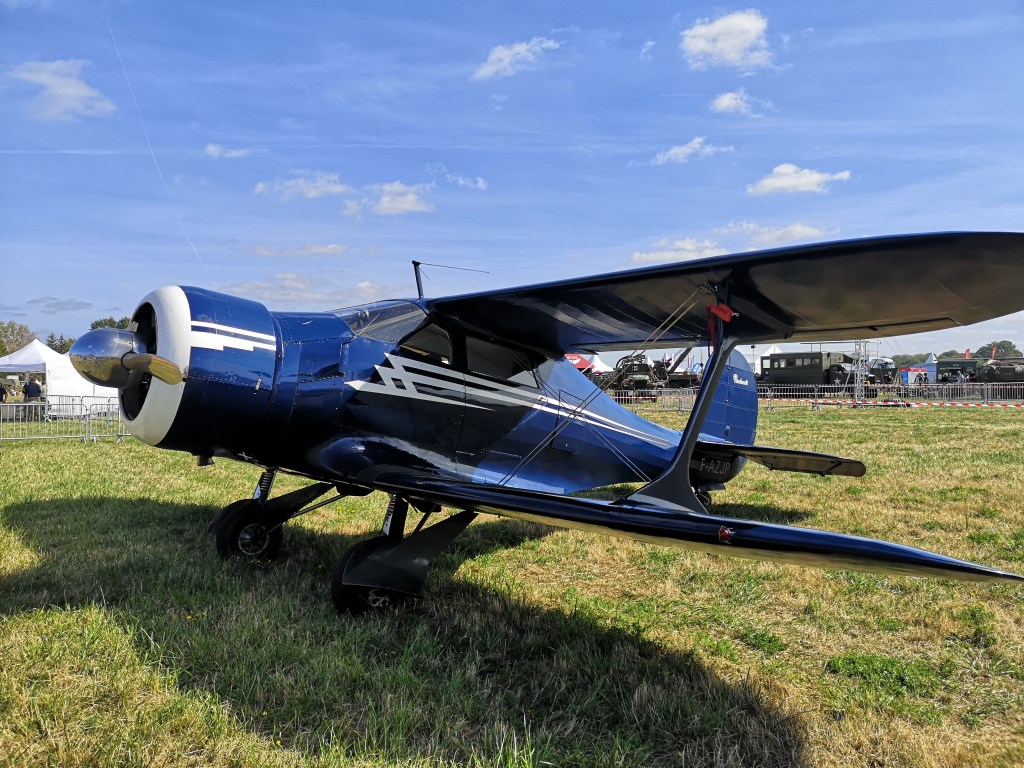 Een blauwe sportvliegtuig met een propeller, geparkeerd op een grasveld onder een blauwe lucht.