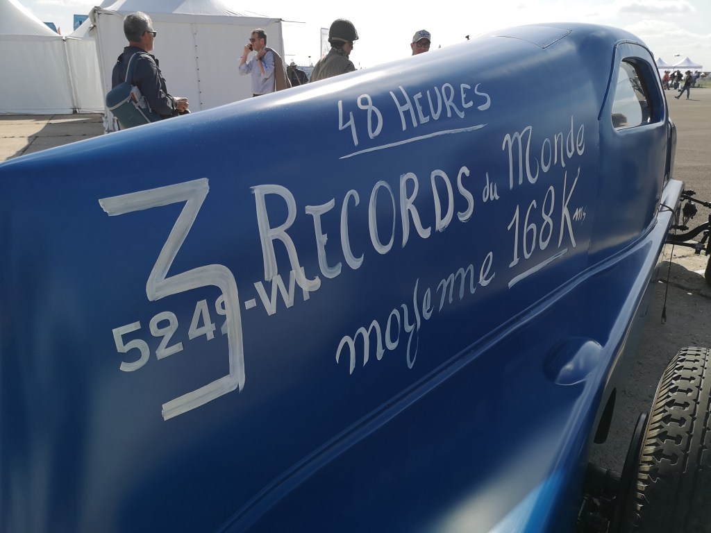 Zijaanzicht van een blauw voertuig met opschriften over wereldrecords en gemiddelde snelheid van 168 km/u.